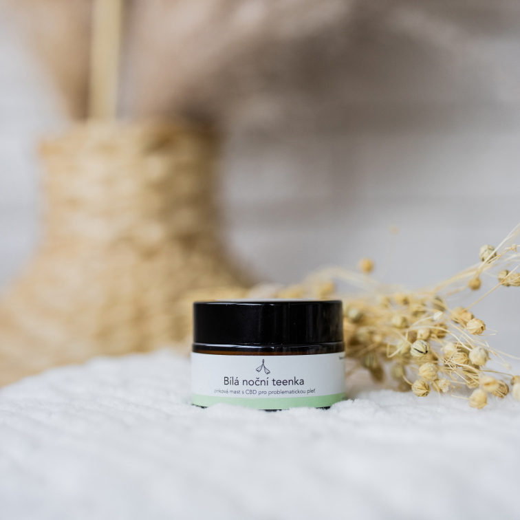 CBD zinkový krém na akné či ekzém, na bílém ubrusu, v pozadí sušené květiny