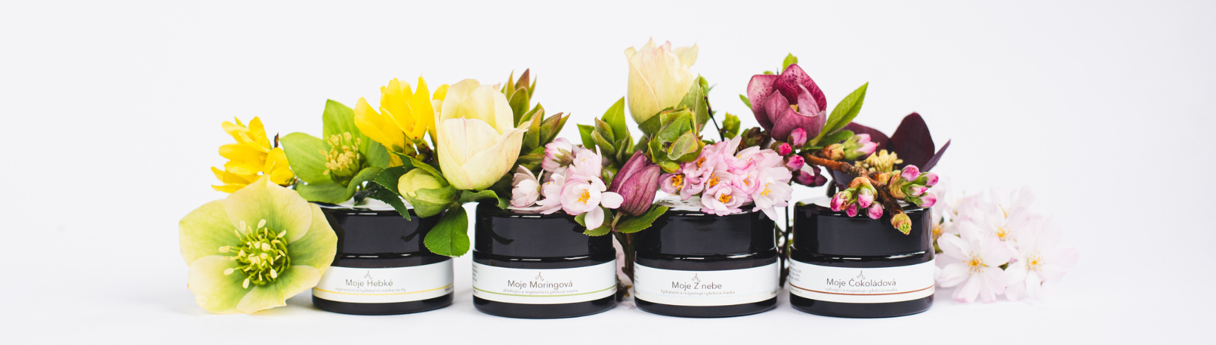 čtyři pleťové masky, na nich jsou položené květy, na bílém pozadí