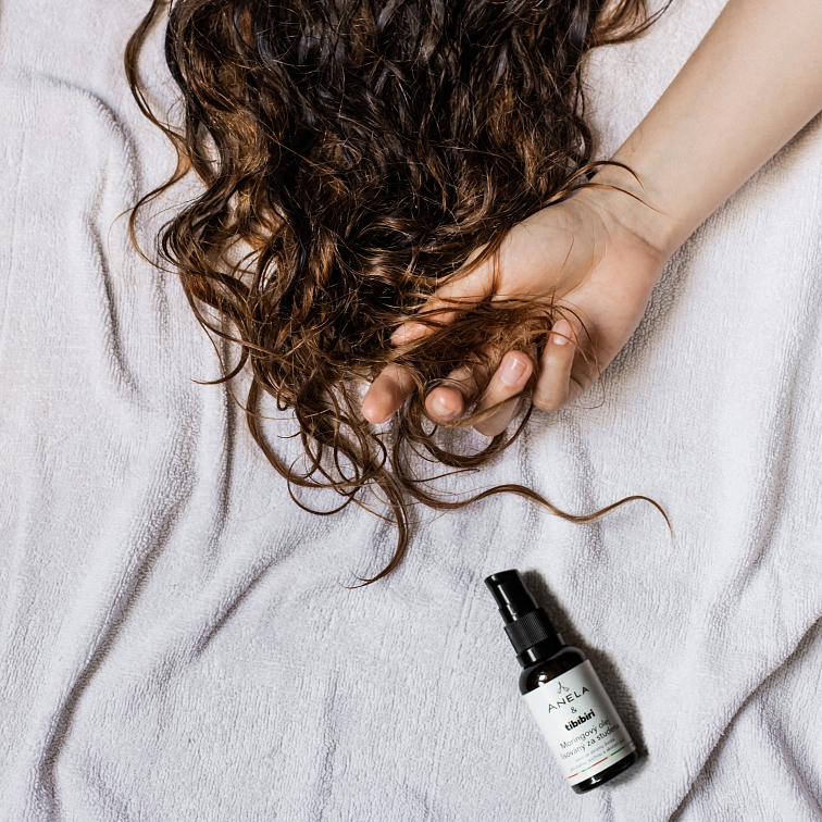 vlasy rozložené na bílém prostěradle, vedle nich položená ruka a moringová olej