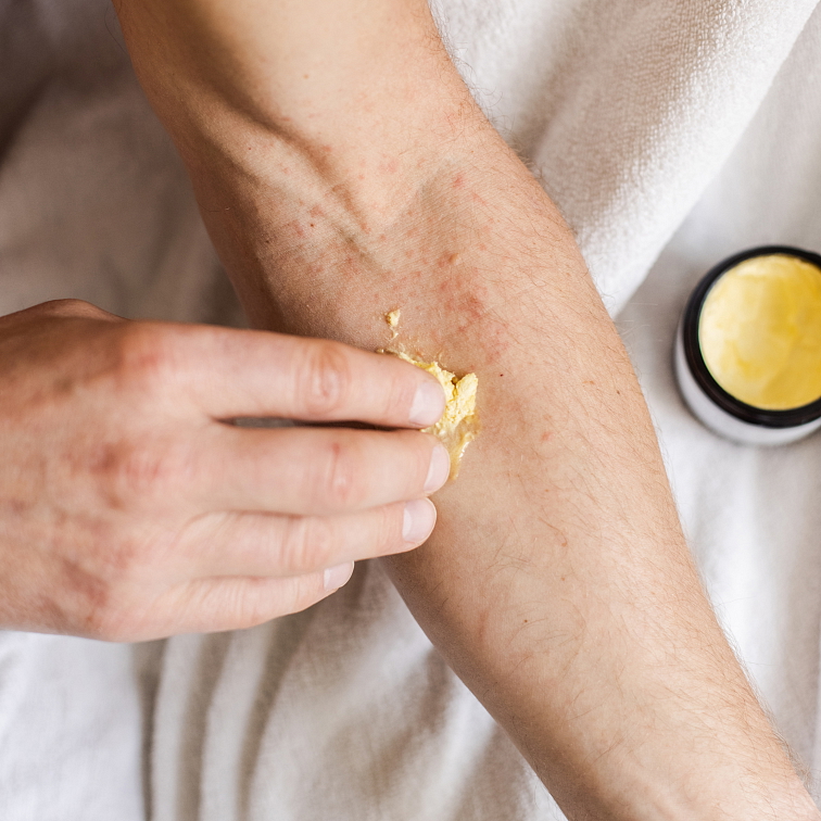 ruka nanášející na předloktí šlehané máslo