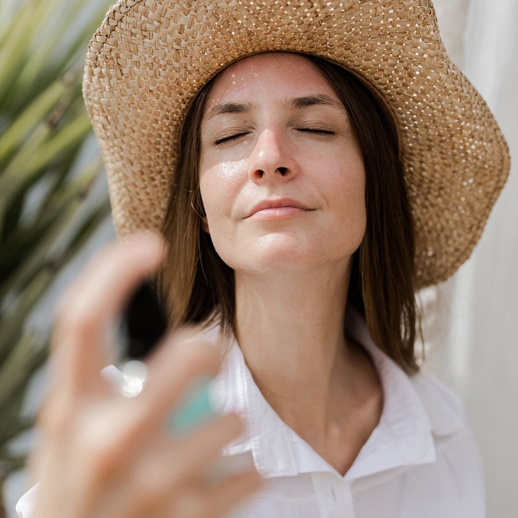 žena v klobouku, která si nanáší na obličej hydratační mlhu Modré z nebe