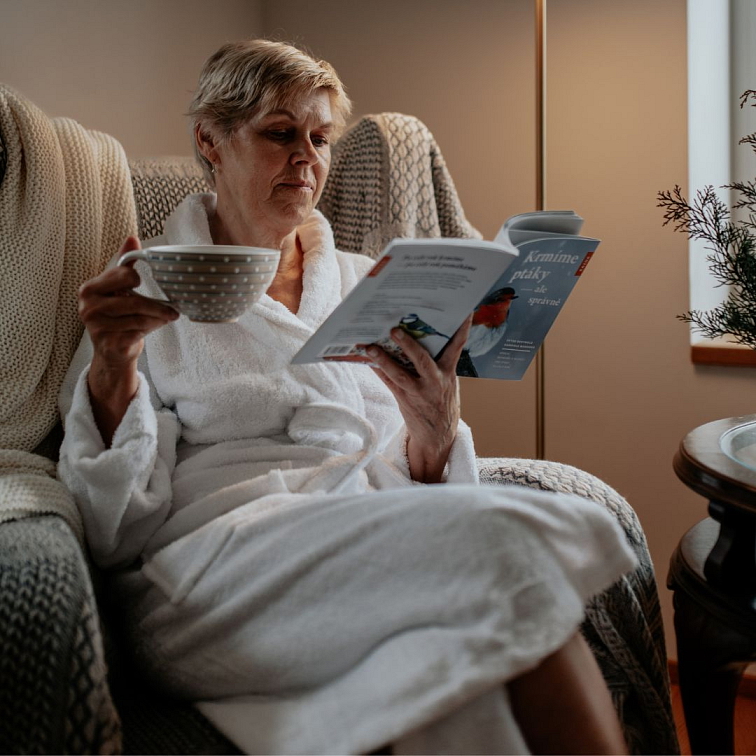 žena na křesle, v jedné ruce drží hrnek, v druhé ruce knihu