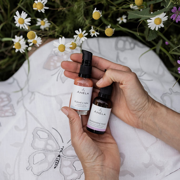 ruce držící hydratační a olejové sérum, nad bílou dekou, okolo jsou drobná kvítka