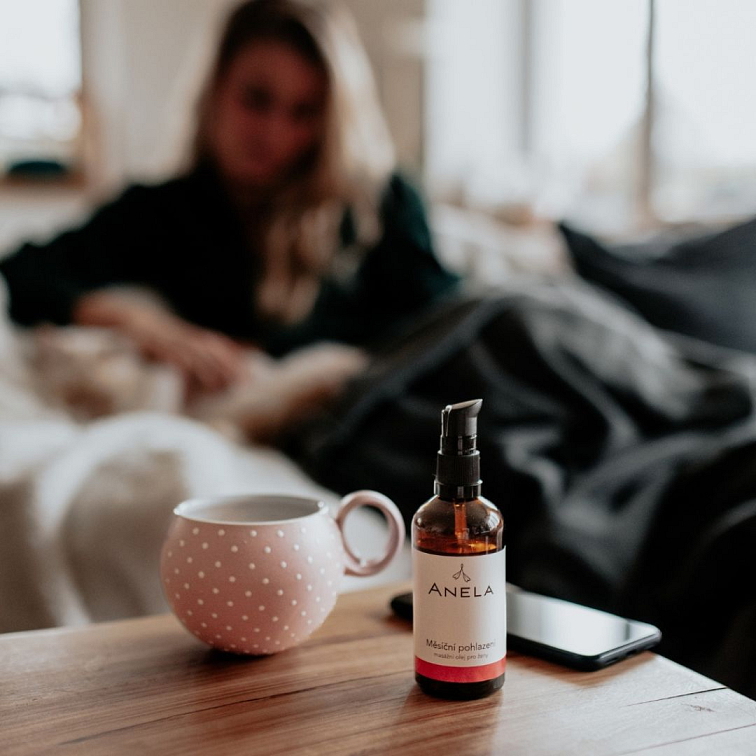 žena v pozadí, v popření hrnek a lahvička s masážním olejem pro ženy s menstruací