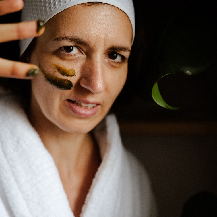 žena v županu, mající na tváři pleťovou masku Moje moringová, na prstech má masku také