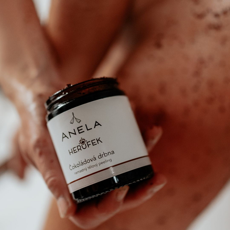 ruka držící peeling Čokoládová drbna, v pozadí ženská noha 