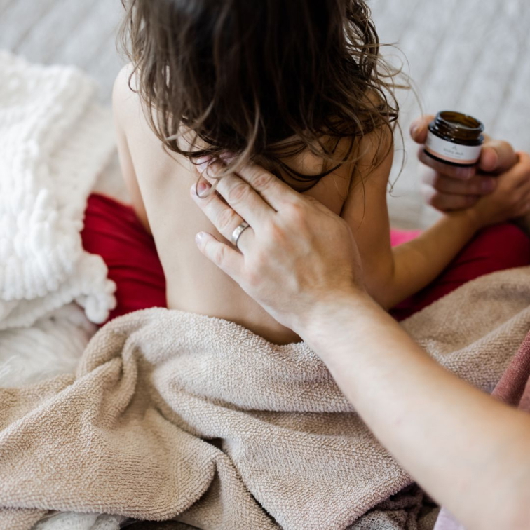 dospělá ruka nanášející dětský prsní balzám na dětská zádíčka