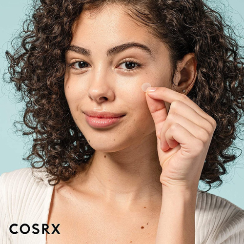 Dívka s krásnou pletí právě sundavá z obličeje expresní náplast proti akné - Master Patch Basic. Její pleť je nyní hladká a bez pupínků. V levém dolním rohu je vidět název korejské značky COSRX.